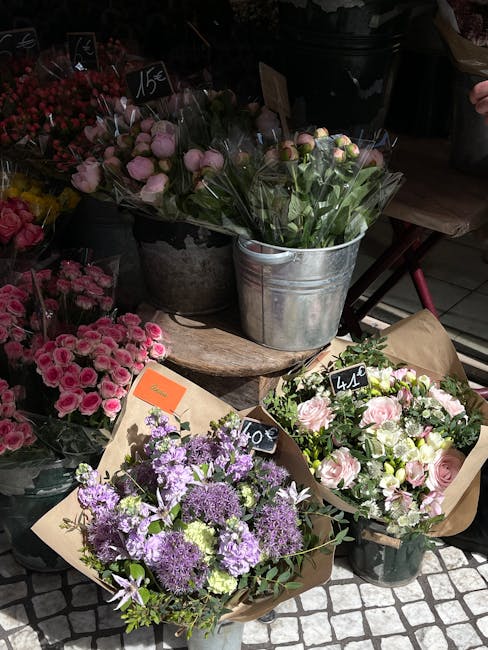 A display of fresh floral arrangements and bouquets at a flower stall on Uxbridge High Street, arranged in various containers including a silver metal bucket and wrapped in brown paper. The bouquets f